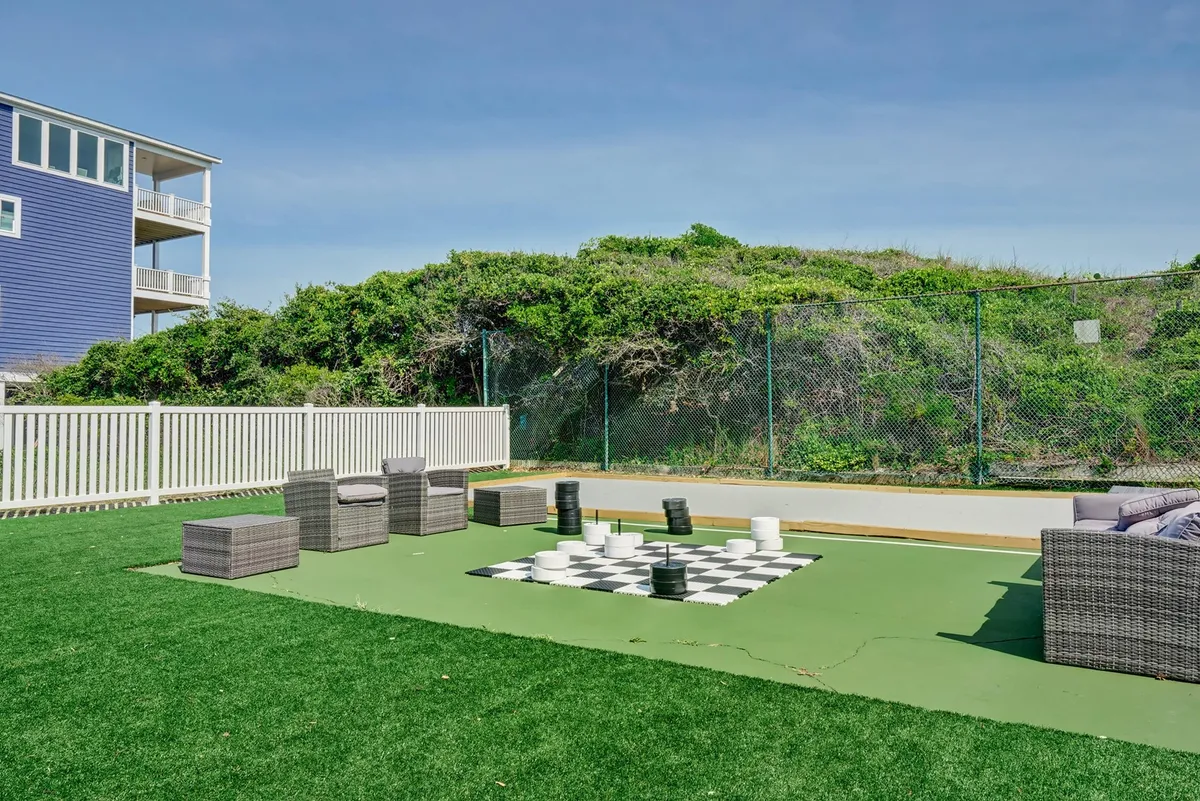 This exterior scene features a large outdoor chessboard, comfortable seating, green grass, and surrounding landscaping. The area invites socializing, light activity, and contemplation in the sun.