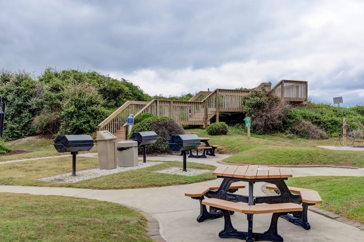 An inviting outdoor grilling and picnic area with several grill stations and picnic tables set against lush greenery. The space is designed for socializing, family barbecues, and relaxing afternoons, echoing the communal and family-focused atmosphere described in the section.