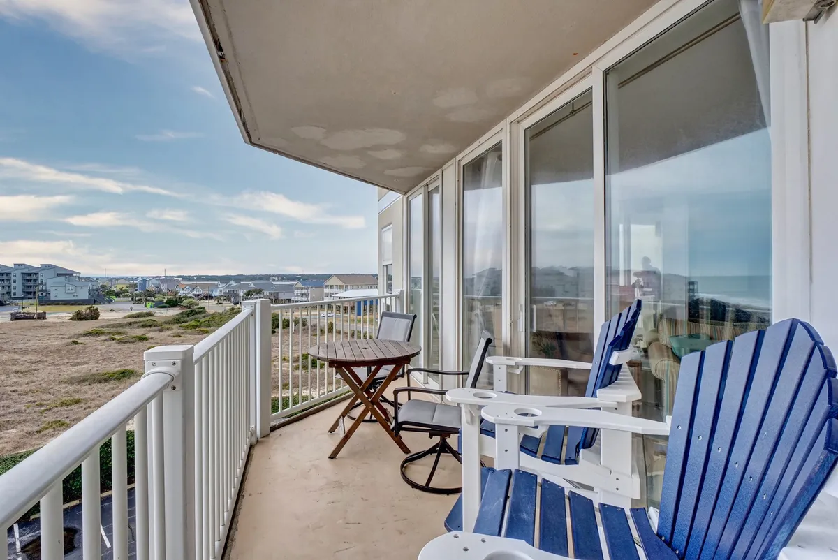 A private balcony with cozy chairs and a small table overlooks a sweeping landscape, likely the ocean. The tranquil scene suggests a perfect spot to start the day with coffee or relax during sunset, encapsulating privacy and romance.