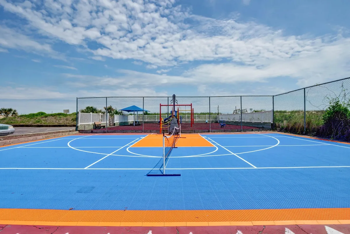 A lively outdoor area featuring a brightly colored basketball court, a tennis net, and playground equipment in the background. Children are seen playing, and the overall mood is energetic and playful, perfectly depicting the range of outdoor activities available for families at the resort.