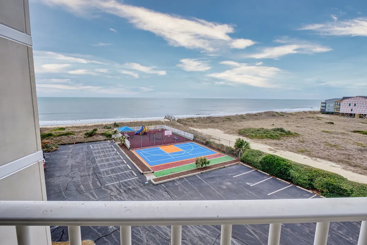 A colorful outdoor basketball court and a vibrant playground set against an ocean backdrop, with families and children actively playing and enjoying the outdoors. The scene is relaxed and joyful, capturing both adult and kid-friendly activities.
