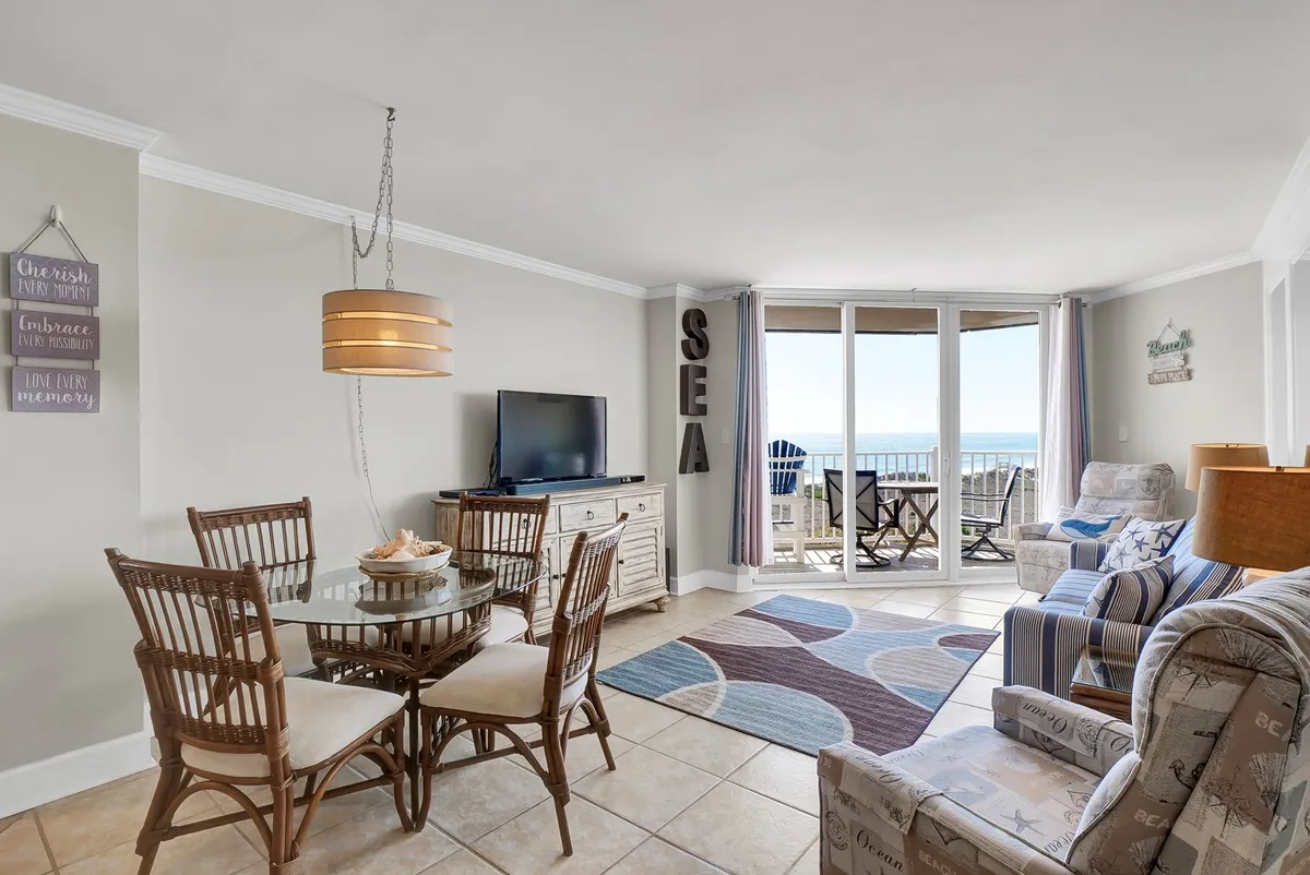 A cozy dining table set near large sliding glass doors, framing a sweeping view of the ocean. The setup is ideal for family meals or romantic dinners, with natural light pouring in and the blue of the sea as a constant backdrop.