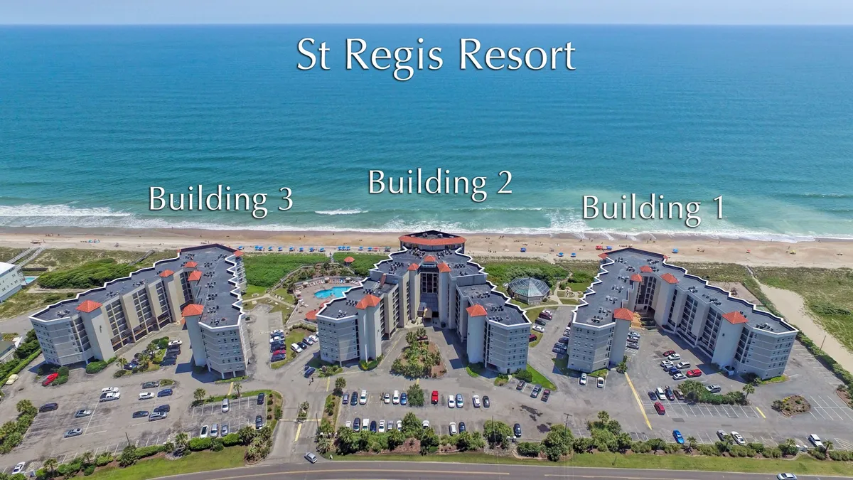A wide shot of the resort’s three main buildings, large swimming pool, and the ocean beyond. The image conveys leisure and relaxation, highlighting the amenities available for a romantic retreat, such as the pool and proximity to the beach.