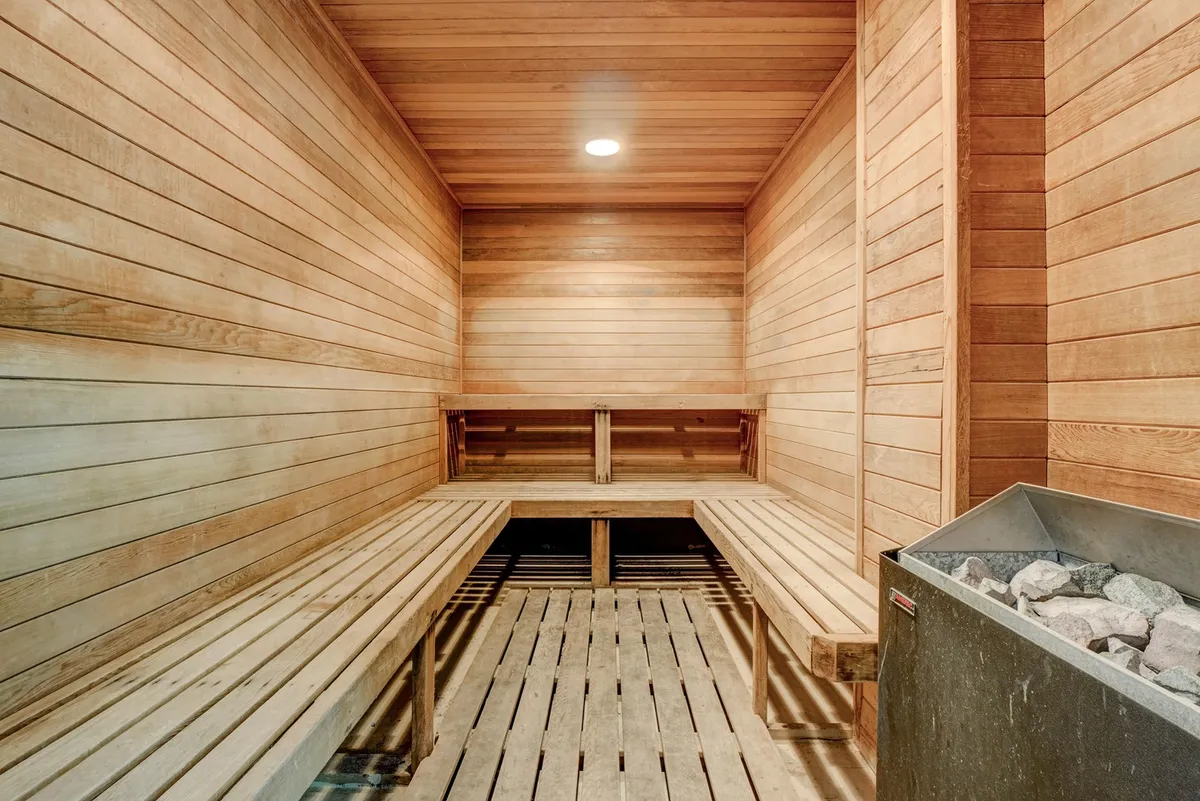 A serene sauna space with wooden benches and classic sauna heater, surrounded by soothing wood paneling. The calm ambiance invites relaxation and a sense of transformative escape.